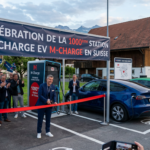 Banner reads “CÉLÉBRATION DE LA 1000ème STATION DE CHARGE EV M-CHARGE EN SUISSE” as people celebrate beside an M-Charge station and electric cars.